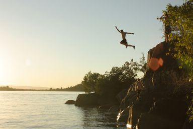 Person jumping from a cliff into calm water, in sunset